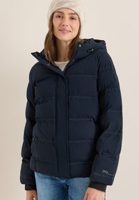 Marinblå puffjacka med dragkedja fram, huva och horisontell quiltning. Har en logotyp på ärmen och ett mjukt, texturerat tyg.