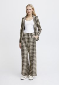 Karierte Blazer und weite Hosen in Beige und Schwarz. Glattes Material mit klassischem Hahnentrittmuster. Weißes Tanktop darunter.