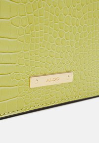 Limegrön konstläderväska med krokodilstruktur och en guld ALDO-logoplåt. Har kontrasterande svarta sömmar runt kanterna.