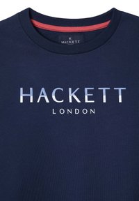 Navy pamučna majica s okruglim izrezom. Ima natpis "HACKETT" i "LONDON" ispisan bijelom bojom, uz kontrastni crveni detalj na unutrašnjem izrezu.