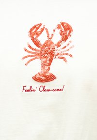 Κόκκινος αστακός με παγιέτες και το κείμενο «Feelin' Claw-some!» κεντημένο από κάτω σε λευκό υφασματικό φόντο.