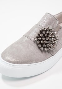Basket slip-on gris clair avec texture scintillante et un regroupement de perles facettées gris foncé sur la tige, semelle épaisse blanche.