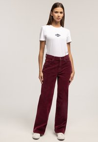 Bordowe szerokie spodnie z sztruksu o teksturowanym wykończeniu, zestawione z dopasowanym białym t-shirtem z małym logo na piersi.