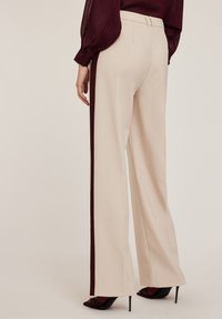 Beige wijde broek met een kastanjebruine zijstreep, gestructureerde tailleband met twee tabs en een soepele stof. Sleehakken zijn zichtbaar.