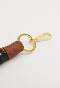 Lædernøgleholder med en brun læderfletning, en gylden cirkelring og en gylden clips. Tekstureret overflade med fremhævede syninger.