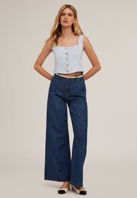 Top scurt de culoare bleu deschis, cu decolteu pătrat și nasturi din lemn, asortat cu pantaloni largi din denim închis la culoare și balerini alb-negru.