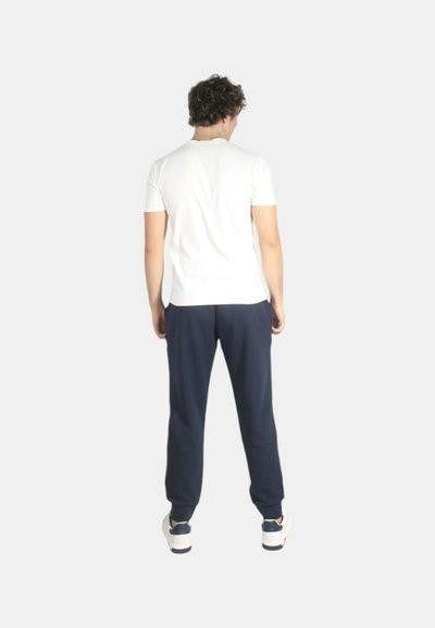 T-shirt bianco a maniche corte e pantaloni della tuta blu navy. La t-shirt è aderente; i pantaloni hanno una vita elastica. Il modello è visualizzato di spalle.