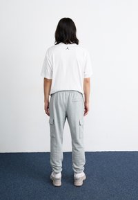 Gray cargo sweatpants with side pockets, paired with a white t-shirt featuring a small black logo on the back. Casual fit, clean design.
