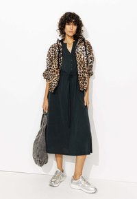 Robe midi noire avec des boutons, taille cintrée. Veste en imprimé léopard marron et noir, sac gris, et baskets argentées complètent le look.