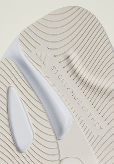 Bėgimo batų padas su tekstūruota šviesiai smėline guma, turintis banginę raštą, baltus akcentus ir įspaustą logotipą "STELLA McCARTNEY".