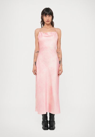 Mouwloze roze maxi-jurk met een gladde, glanzende textuur en subtiel gemarmerd patroon. Gestyled met zwarte leren enkellaarsjes.