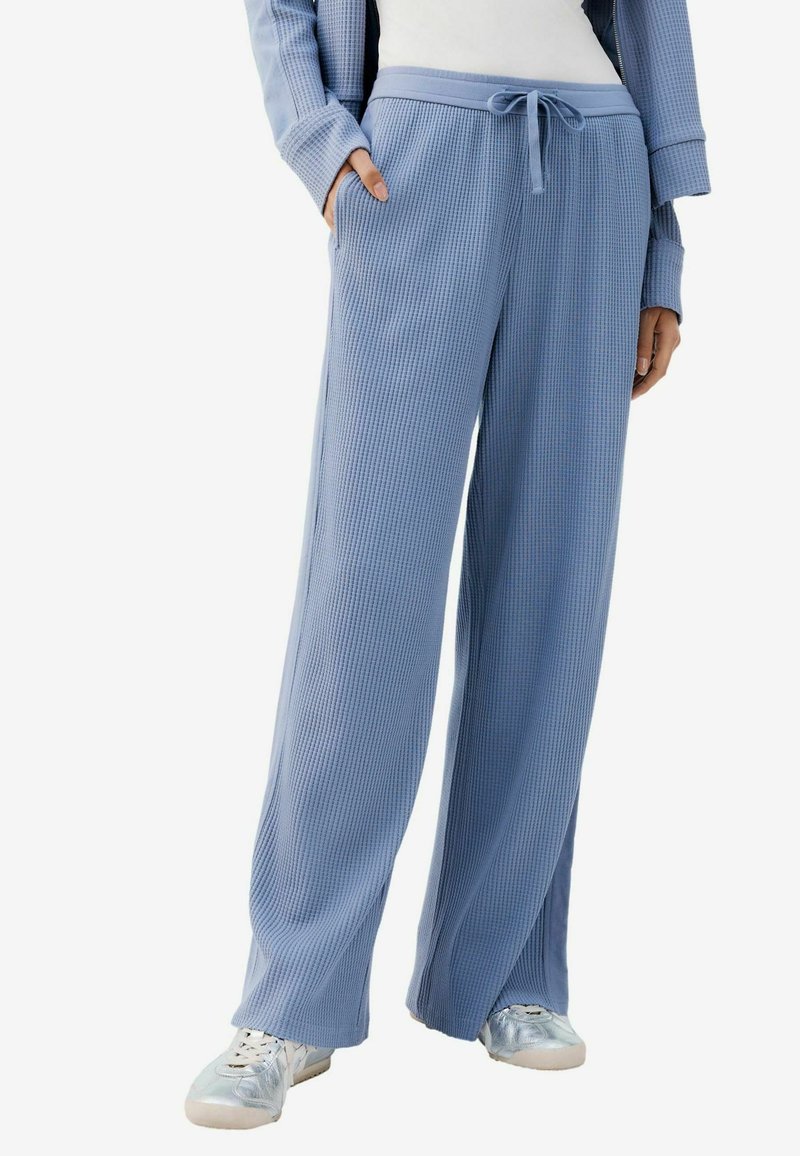 Pantalones de pierna ancha color azul claro en una tela con textura acanalada. Presentan una cintura elástica con cordón y bolsillos laterales.