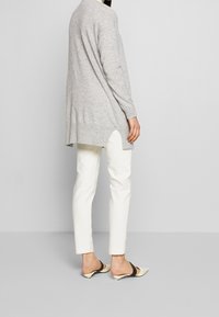 Ljust grå, långärmad stickad cardigan med sidofickor, tillsammans med slim fit vita byxor och svarta och beige öppna tåklackar.