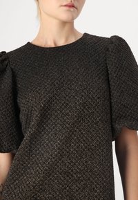 Černý texturovaný top s jemným metalickým leskem, který má krátké nabírané rukávy a kulatý výstřih, vyrobený z tkaného materiálu.