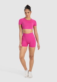 Pink atletisk todelt sæt med en tætsiddende crop top med korte ærmer og højtaljede shorts, lavet af et elastisk, glat stof.