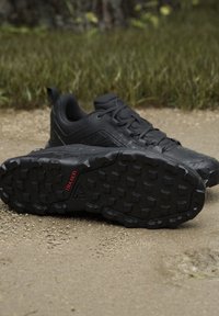 Scarpe da trekking nere con suole robuste etichettate "TRAXION" su un sentiero di terra con erba sullo sfondo.