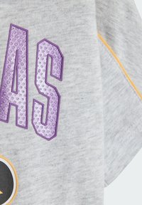 Szara bawełniana koszulka z fioletowymi teksturowanymi literami i okrągłym czarnym logo z pomarańczową obwódką, umieszczonym na przedniej stronie.