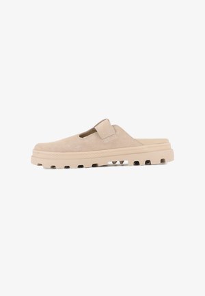 Chaussure slip-on en suède beige avec une semelle plate et texturée ainsi qu'une sangle velcro. Elle présente un bout arrondi et des découpes sur les côtés pour la respirabilité.