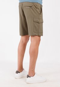 Pantaloni cargo verde oliva in tessuto testurizzato, con tasche laterali e una tasca posteriore con zip, abbinati a sneaker bianche e accenti grigi.