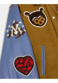 Bruine wolmix jas met blauwe leren mouwen, voorzien van multifunctionele patches: berengezicht, "M" logo, sterren en een rood hart ontwerp.