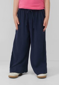 Marineblaue, weit geschnittene Hosen aus strukturiertem Stoff, mit einem elastischen Bund und Kordelzug sowie Seitentaschen. Kombiniert mit weißen Schuhen.