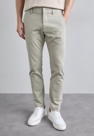 Light green chinos with a slim fit and smooth texture, paired with white low-top sneakers. Features a discreet front pocket design.