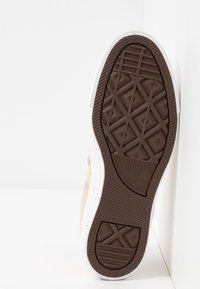 Brun gummisul med geometriska mönster, med en vit mellansula. Sidan har orange och vita sprutande detaljer. Converse-logotyp synlig.