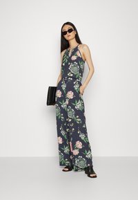 Macacão floral em azul-marinho com design sem mangas, apresentando um recorte em forma de buraco de chave. Decorado com padrões de flores rosas e verdes, com silhueta de pernas largas.