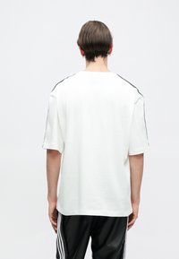 White short-sleeve t-shirt with black side accents and a relaxed fit, made of soft cotton fabric. Minimalist design, back view.