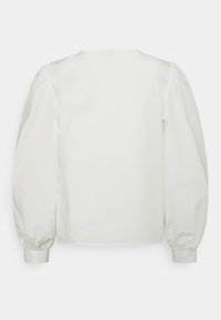 Blusa de algodão branca com decote redondo, mangas longas bufantes e punhos ajustados. Textura suave e design simples.