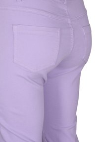 Violett stretchbuxur með fitaðri hönnun, með tveimur bakpokum og sýnilegum saummun. Efnið virðist slétt og létt.