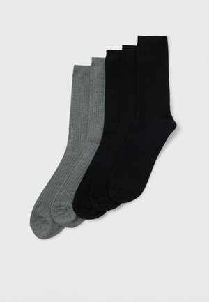 Deux paires de chaussettes en coton à côtes, l'une grise et l'autre noire, soigneusement alignées sur un fond blanc.