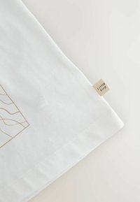 Bílý povlak na polštář s designem zlatého line artu, vyrobený z měkké bavlny, s malou štítkem s textem 'Little Bird' přišitým na okraji.