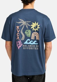 Camiseta de manga corta en color navy con un gráfico colorido que presenta palmeras, sol, olas, un cactus y el texto "Balance de Opuestos."