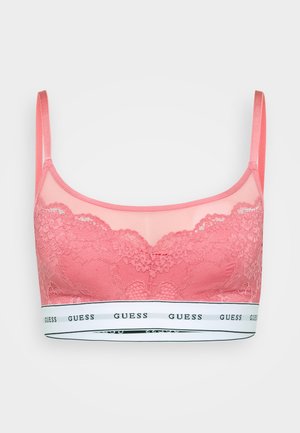 Bralette en dentelle rose avec des panneaux transparents, des bretelles réglables et une bande blanche affichant le logo "GUESS". Texture florale détaillée sur l'ensemble.