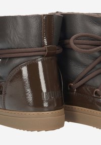 Brown leather boots with a glossy finish, featuring a textured upper, round laces, and a chunky rubber sole. Branding visible on the side.