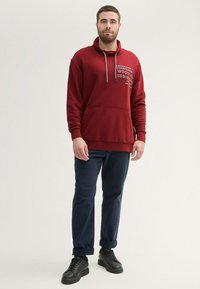 Bordowy kaptur z szarym graficznym napisem, z regulowanym kapturem, kieszenią z przodu, zestawiony z granatowymi spodniami i czarnymi tenisówkami. Gładka faktura materiału.