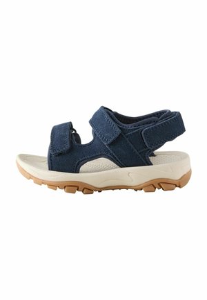 Marineblaue Sandale mit offenem Zehenbereich, verstellbaren Riemen, gepolsterter beiger Sohle und strukturierter brauner Gummilaufsohle für den Außenbereich.