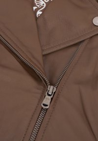 Braune Lederjacke mit einem Metallreißverschluss, die eine glatte Textur und einen umgeschlagenen Kragen aufweist. Innen ist ein gemustertes Material zu sehen.