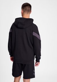 Felpa nera con una finitura testurizzata, caratterizzata da strisce grigie sulle spalle e un cappuccio con cordino. Abbinata a pantaloni corti neri coordinati.