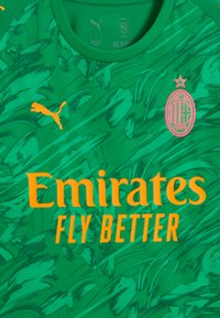 Vihreä urheilupaita, jossa on teksturoitu muotoilu, sisältäen rohkean oranssin "Emirates FLY BETTER" -logon ja vaaleanpunaisen AC Milan -embleemin rinnassa.