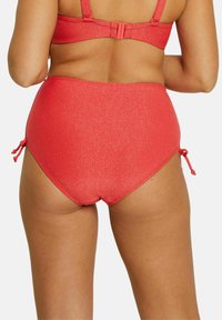 Bas de bikini rouge taille haute avec une texture pailletée, présentant des accents à nouer sur les côtés et une finition lisse.