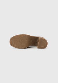 Semelle en caoutchouc marron avec une surface texturée ; design à talon bloc ; matériau durable et flexible ; bord lisse le long de la semelle.