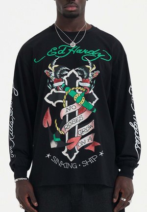 Zwarte langemouwen shirt met een kleurrijk grafisch ontwerp van een kruis, rozen en tekst. De stof lijkt zacht en heeft een ontspannen pasvorm.