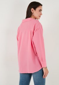 Pink button-up shirt with a textured ribbed fabric, long sleeves, and a classic collar. The back features a yoke and a slightly curved hem.