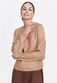 Jasnobrązowy sweter z dzianiny, wykonany z teksturowanej przędzy, charakteryzujący się luźnym fasonem, prążkowanym dekoltem oraz subtelnymi metalicznymi akcentami.