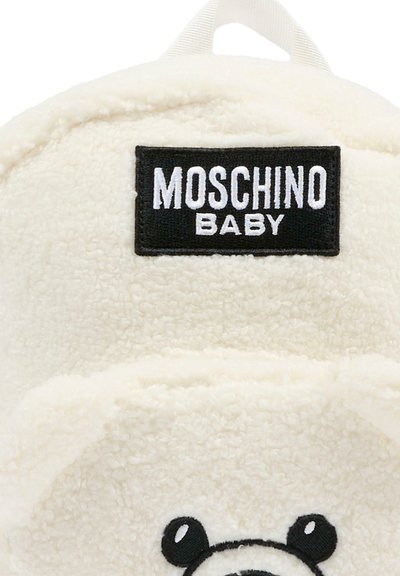 Zaino in peluche bianco con design di faccia d'orso, occhi neri ricamati e etichetta "MOSCHINO BABY" su un rettangolo nero nella parte superiore.