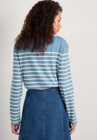 Dlouhý rukáv pruhovaný top v modré a bílé, spárovaný s džínsovou sukní. Má uvolněný střih, kulatý výstřih a zakřivený lem.