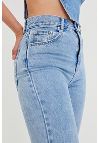 Jeans de mezclilla de tiro alto, color azul claro, con un diseño ajustado, costuras visibles, bolsillos frontales y cierre de cremallera.