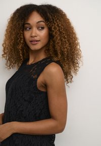 Top en dentelle noire sans manches, avec un motif floral et un col festonné. Texture douce et silhouette ajustée.